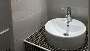 Un baño moderno con azulejos blancos, un lavabo redondo y un espejo.