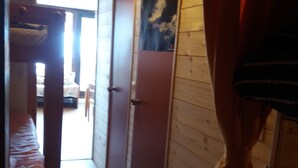 Un pasillo estrecho con paredes de madera y una cama litera a la izquierda. A la derecha, se ven dos puertas, una con un cartel.