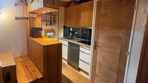 Una cocina compacta con armarios de madera, lavavajillas y una pequeña mesa de comedor.