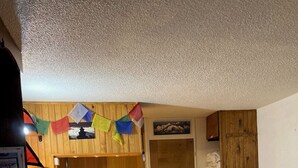 Una cocina compacta con armarios de madera, una pequeña mesa de comedor y una cama con colcha estampada.