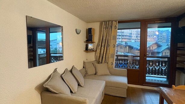 Una sala de estar acogedora con un sofá, una mesa de madera y un ventanal con vistas a edificios.