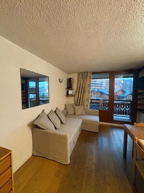 Un salon confortable avec un canapé, une table en bois et une fenêtre donnant sur des immeubles.