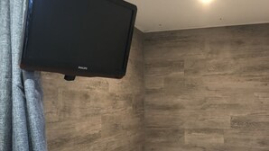 A room with a flat-screen TV mounted on the wall, a bed with a white mattress, and wooden paneling on the walls.