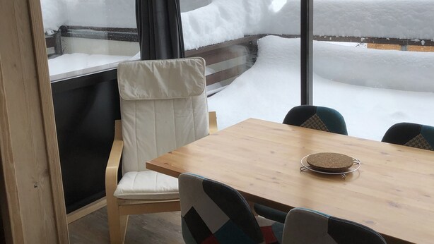 A room with a large window, a wooden table, and two chairs with colorful patterns.