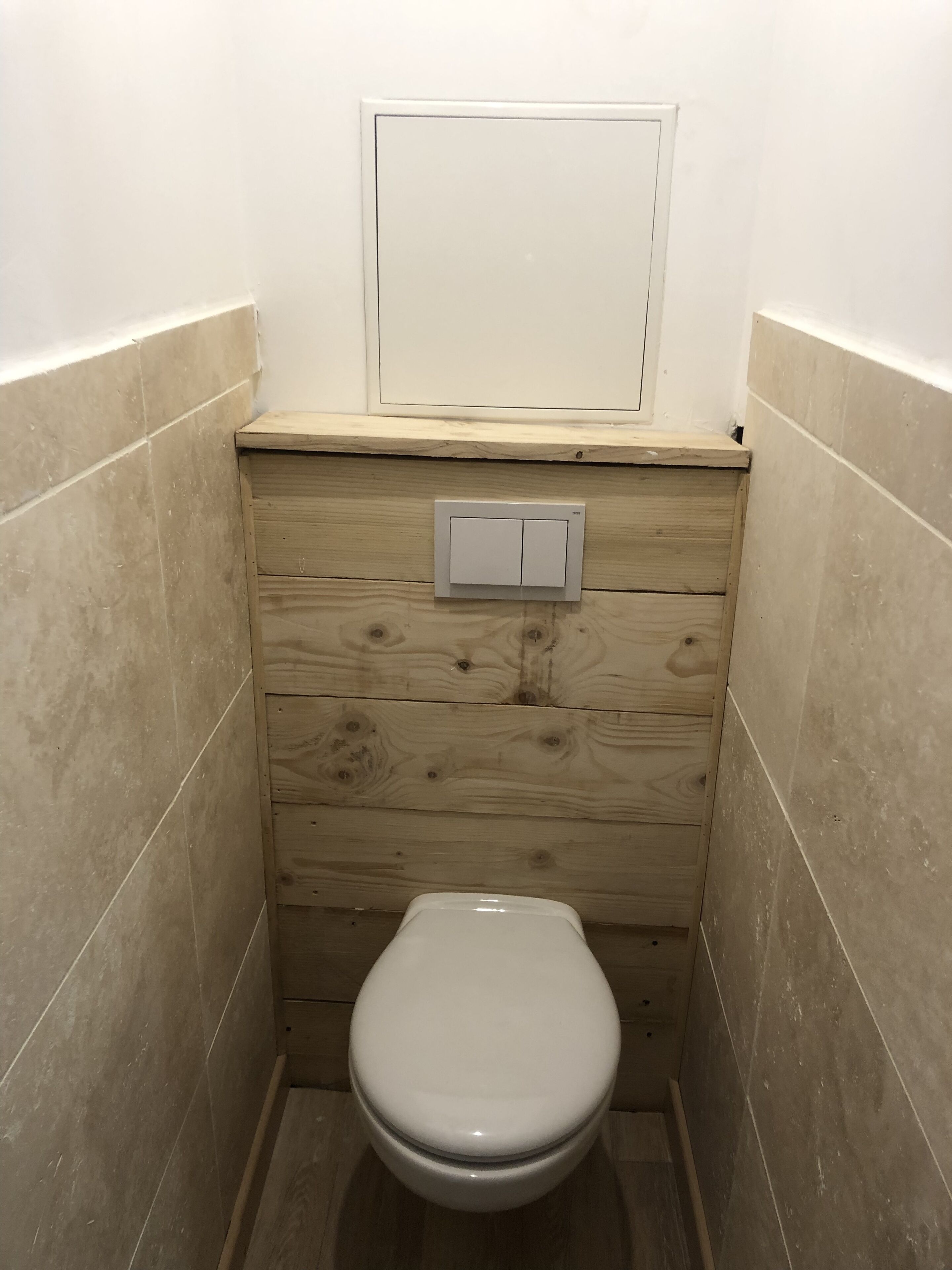 A small, compact bathroom with a wooden vanity, a white toilet, and a wall-mounted light switch.