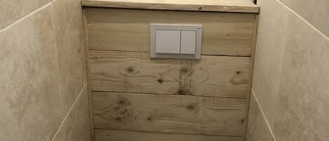 A small, compact bathroom with a wooden vanity, a white toilet, and a wall-mounted light switch.