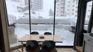 A dining area with a wooden table and chairs, a sofa, and a view of a snowy outdoor scene through large windows.