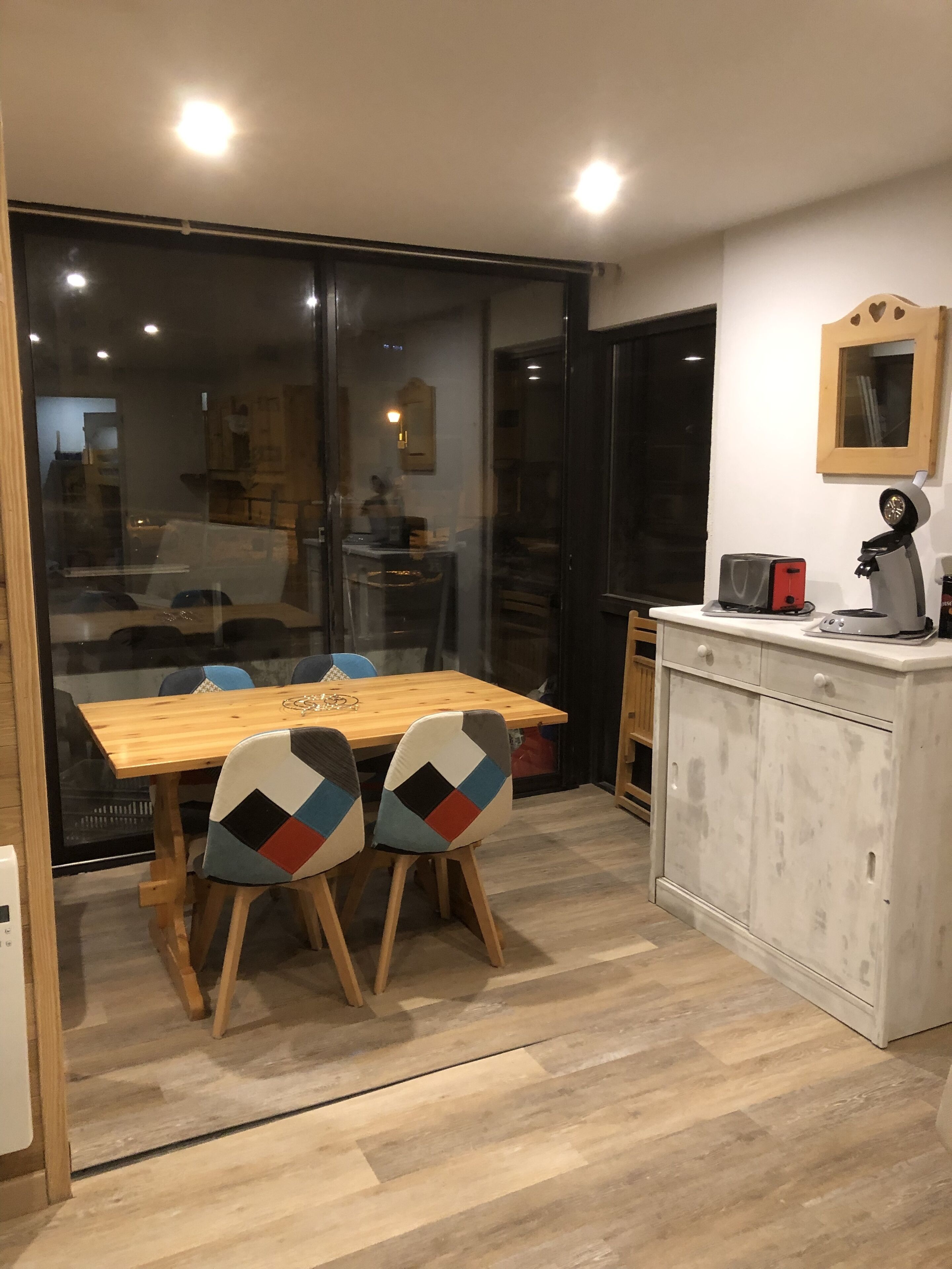 A modern kitchen with a wooden table and chairs, a coffee machine, and a cabinet.