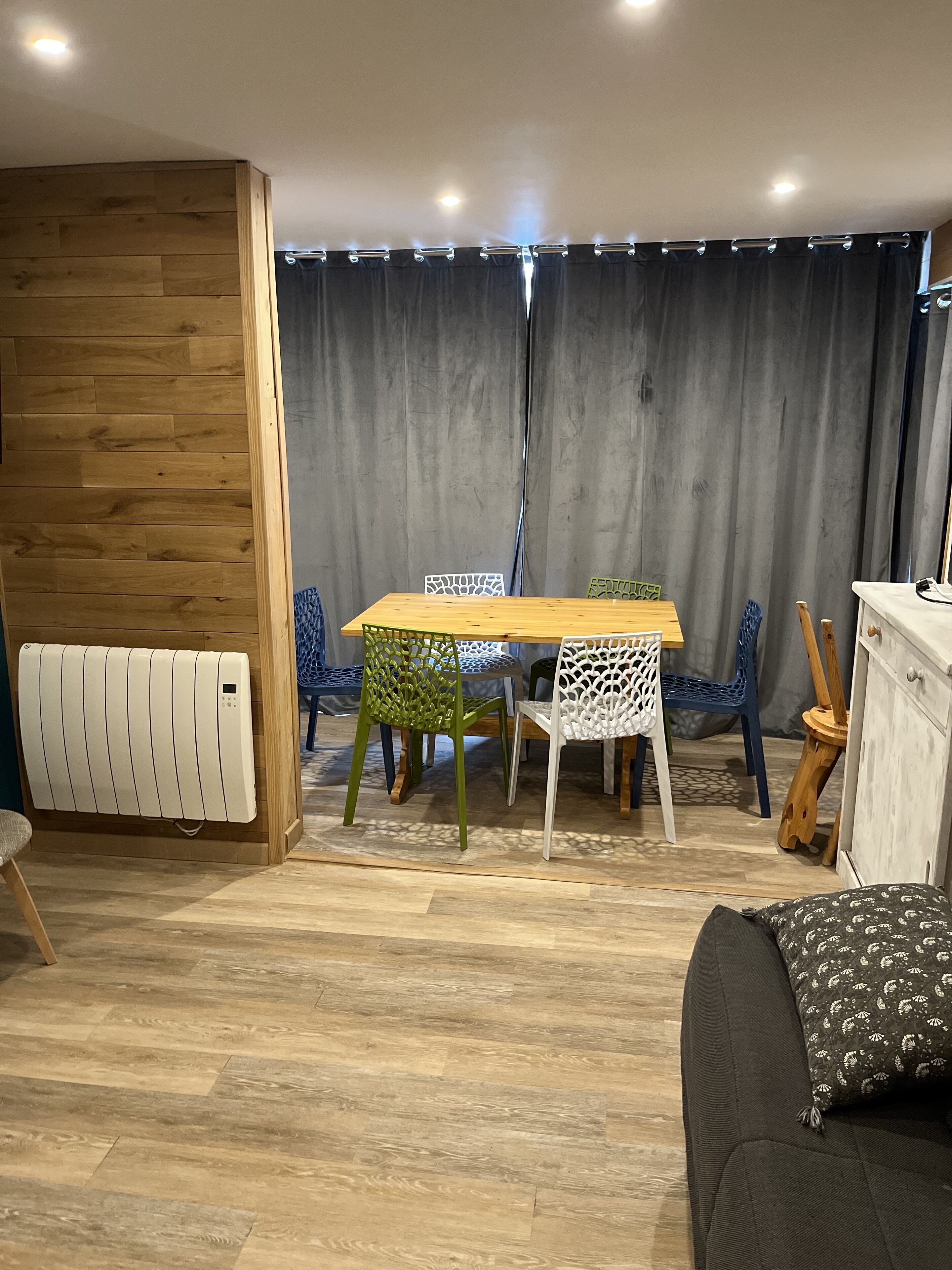 A dining area with a wooden table and chairs, a radiator, and a grey curtain backdrop.