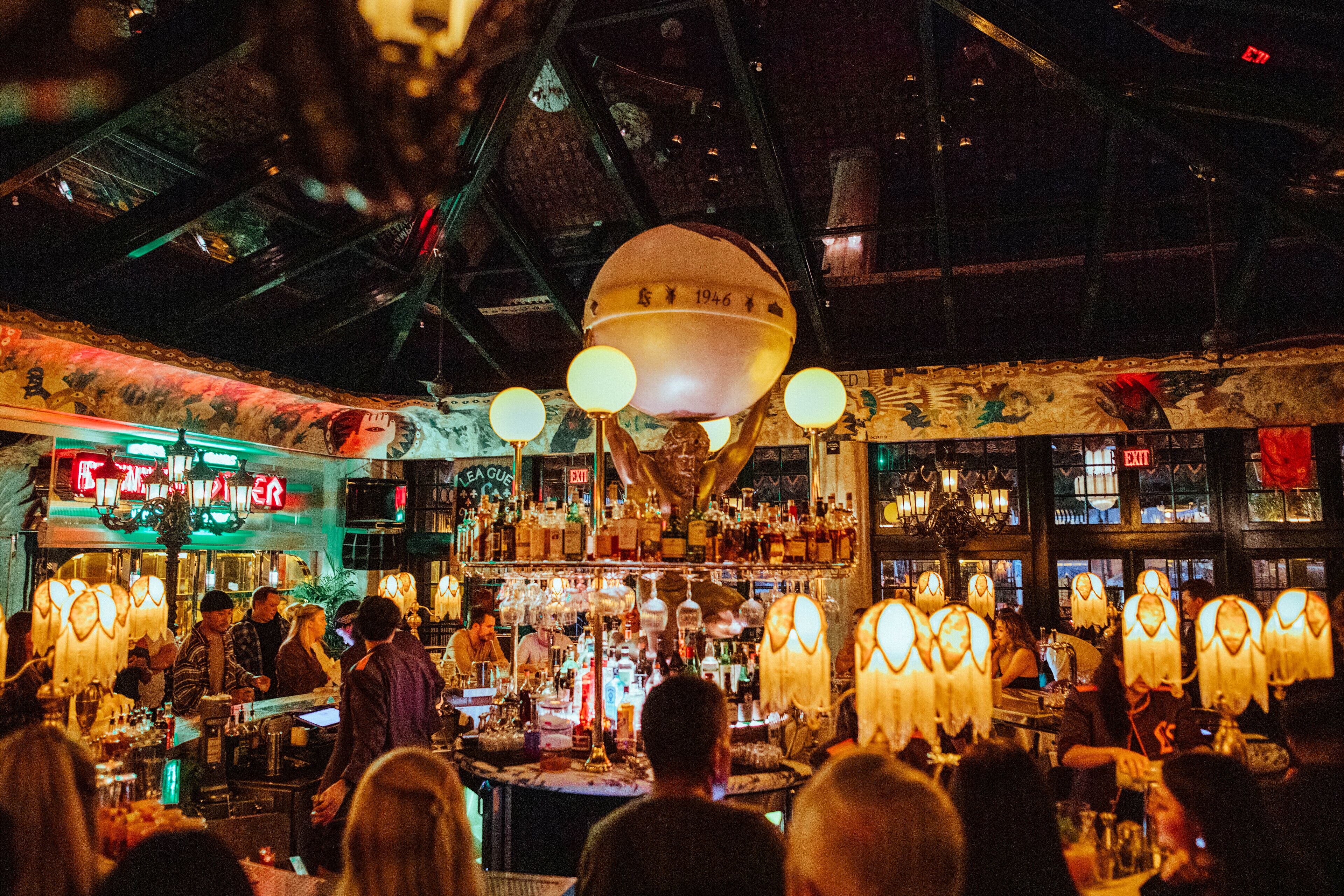 Eine Bar mit hoher Decke und hängenden Lampen, voller Gäste und Barkeeper.