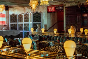 Restaurante com cadeiras estofadas com padrão, área de bar e decoração vintage, incluindo uma placa com a inscrição 'Sala de Reuniões'.