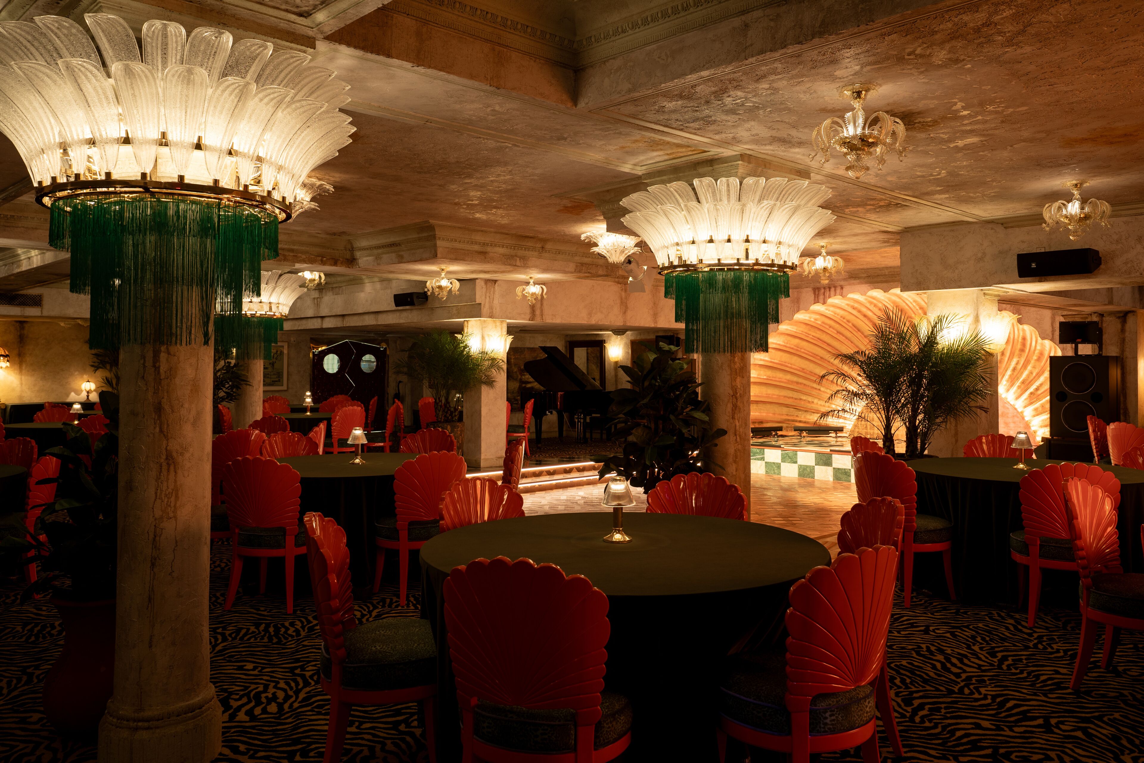 A restaurant with round tables and red chairs, featuring ornate chandeliers and a zebra-patterned floor.