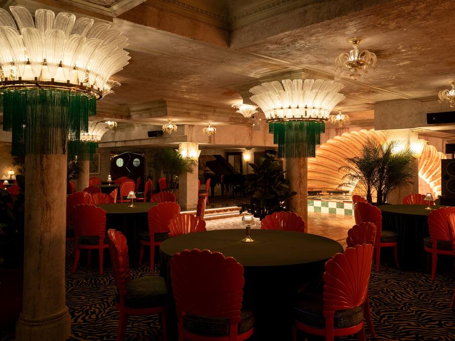 A restaurant with round tables and red chairs, featuring ornate chandeliers and a zebra-patterned floor.