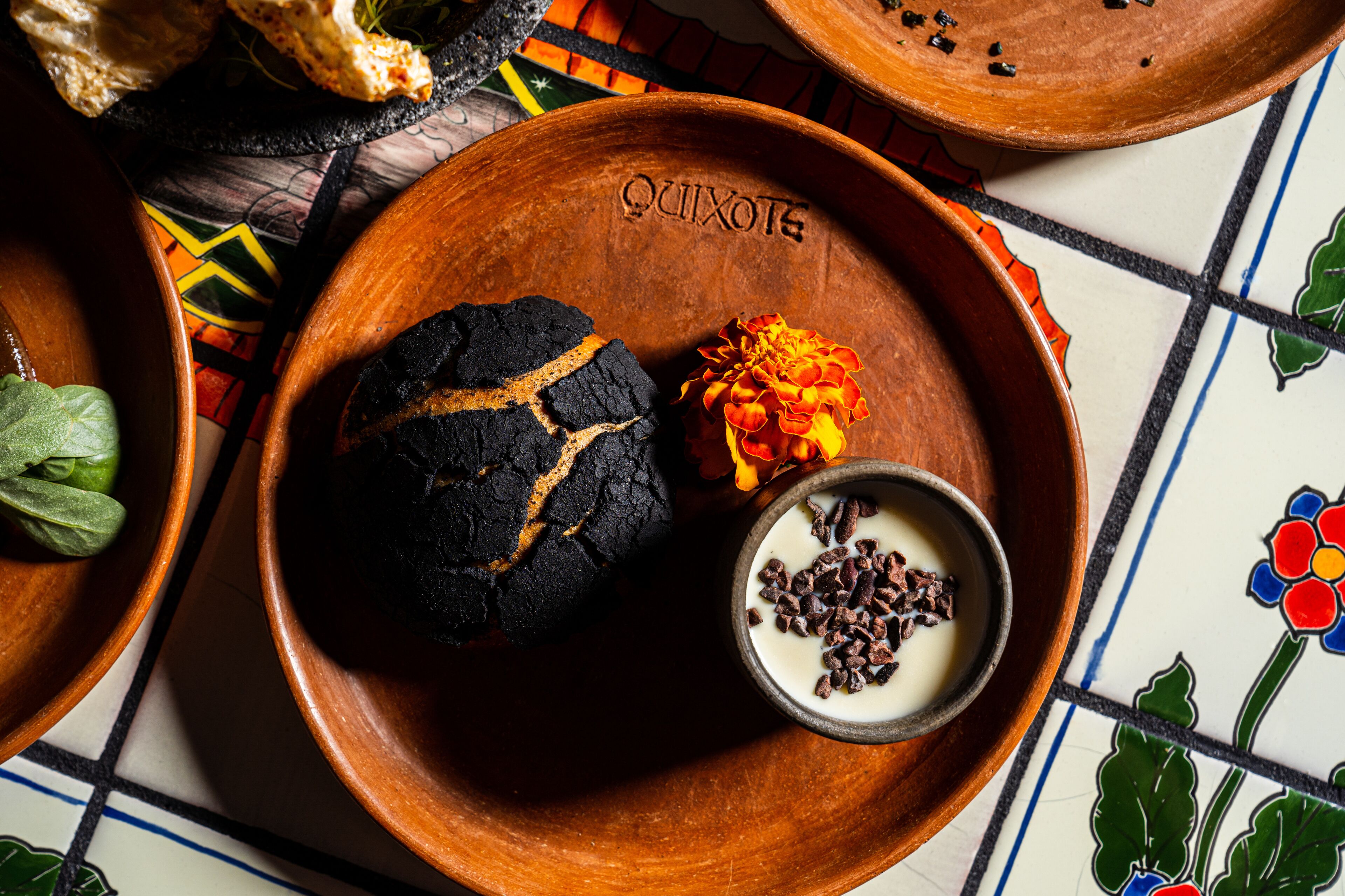 A terracotta plate with a cookie, a small bowl of chocolate, and a flower.