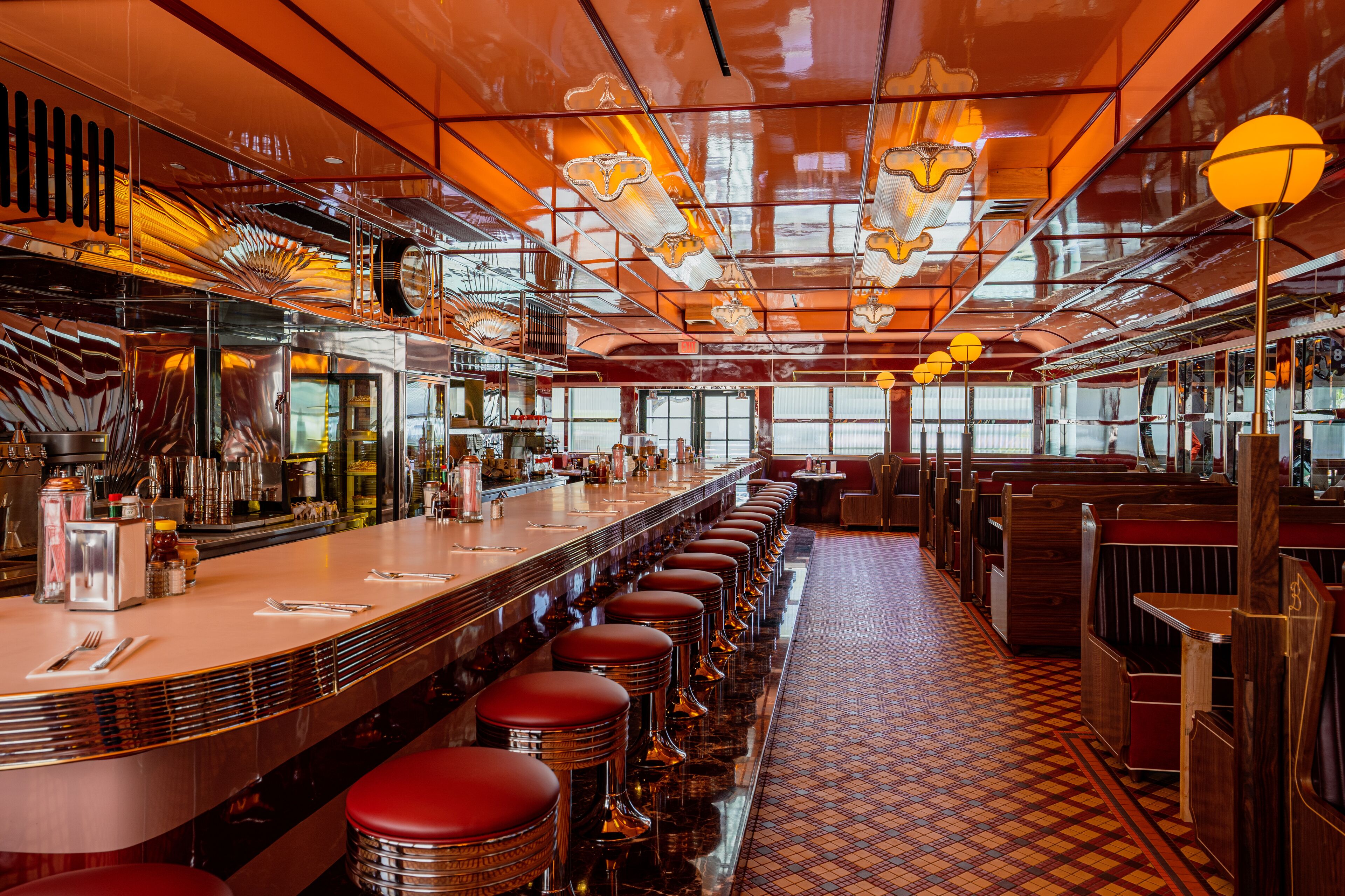 Un restaurant doté d’un long bar, de tabourets rouges et d’un sol à motifs.