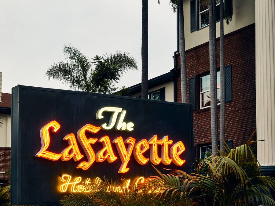 Une enseigne au néon représentant « The LaSayette Hotel & Casino », avec un mur de briques et des palmiers au premier plan.