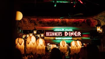 A dimly lit bar with a neon sign reading "BEGINNER'S DINER" and a patterned ceiling.