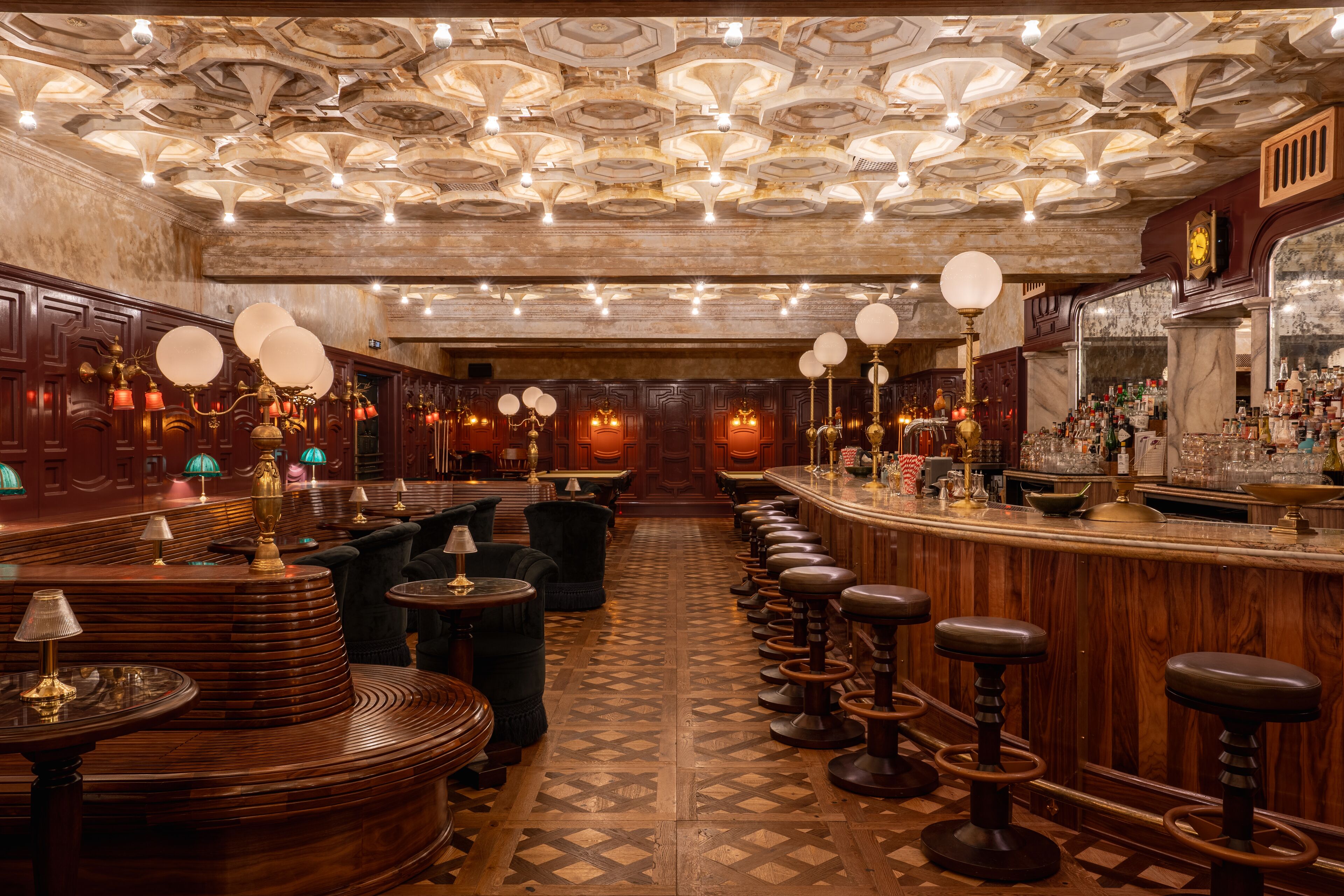 A bar with wooden bar stools, a patterned floor, and a ceiling with ornate designs.