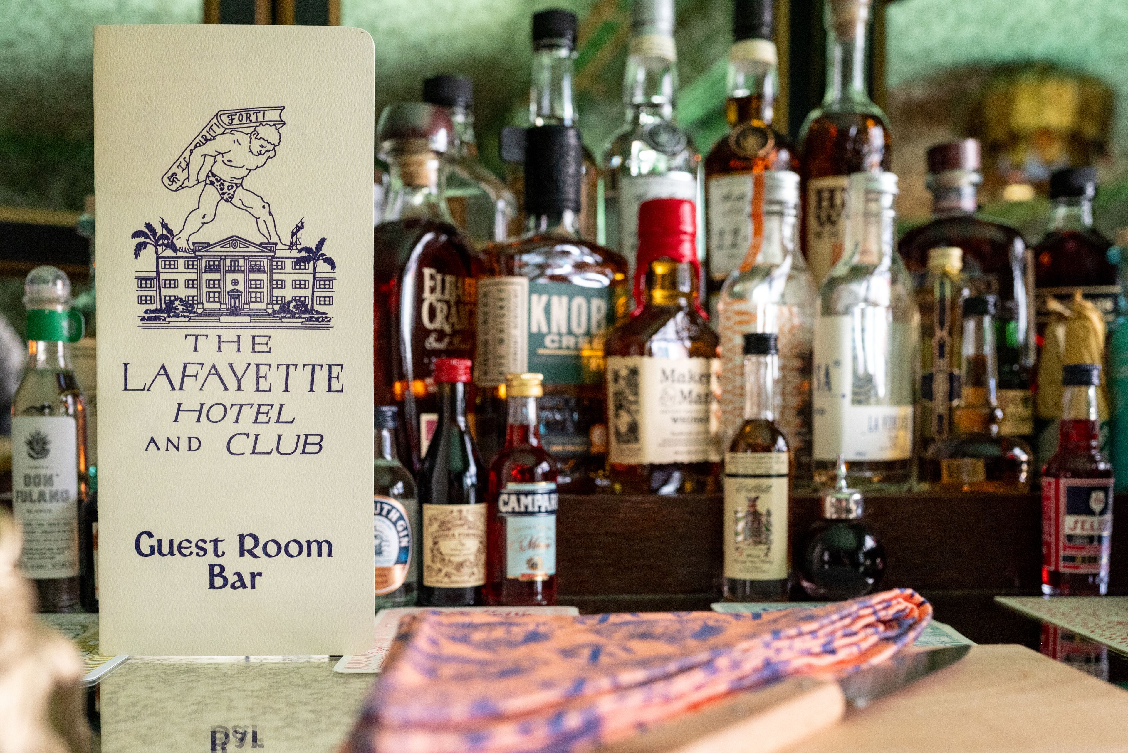Cartell del bar de les habitacions d'hostes de The Lafayette Hotel and Club, envoltat de diverses ampolles de licors.