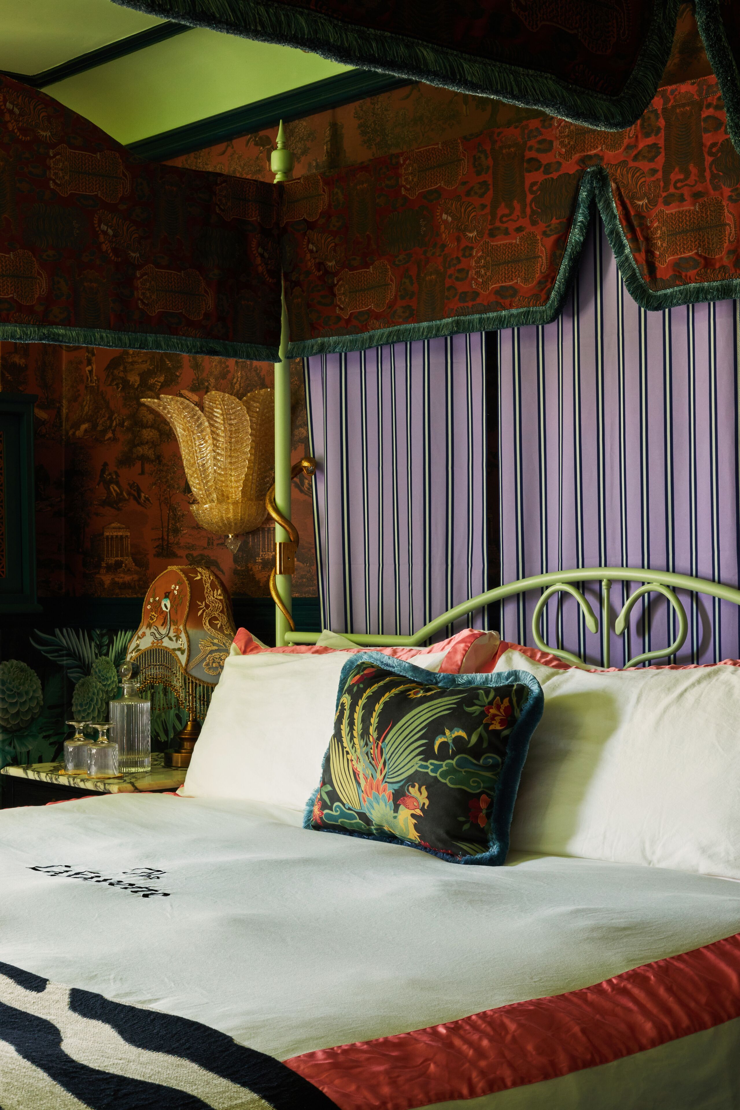 Un dormitorio con cama, almohadas, una mesita de noche y un papel tapiz con diseño.