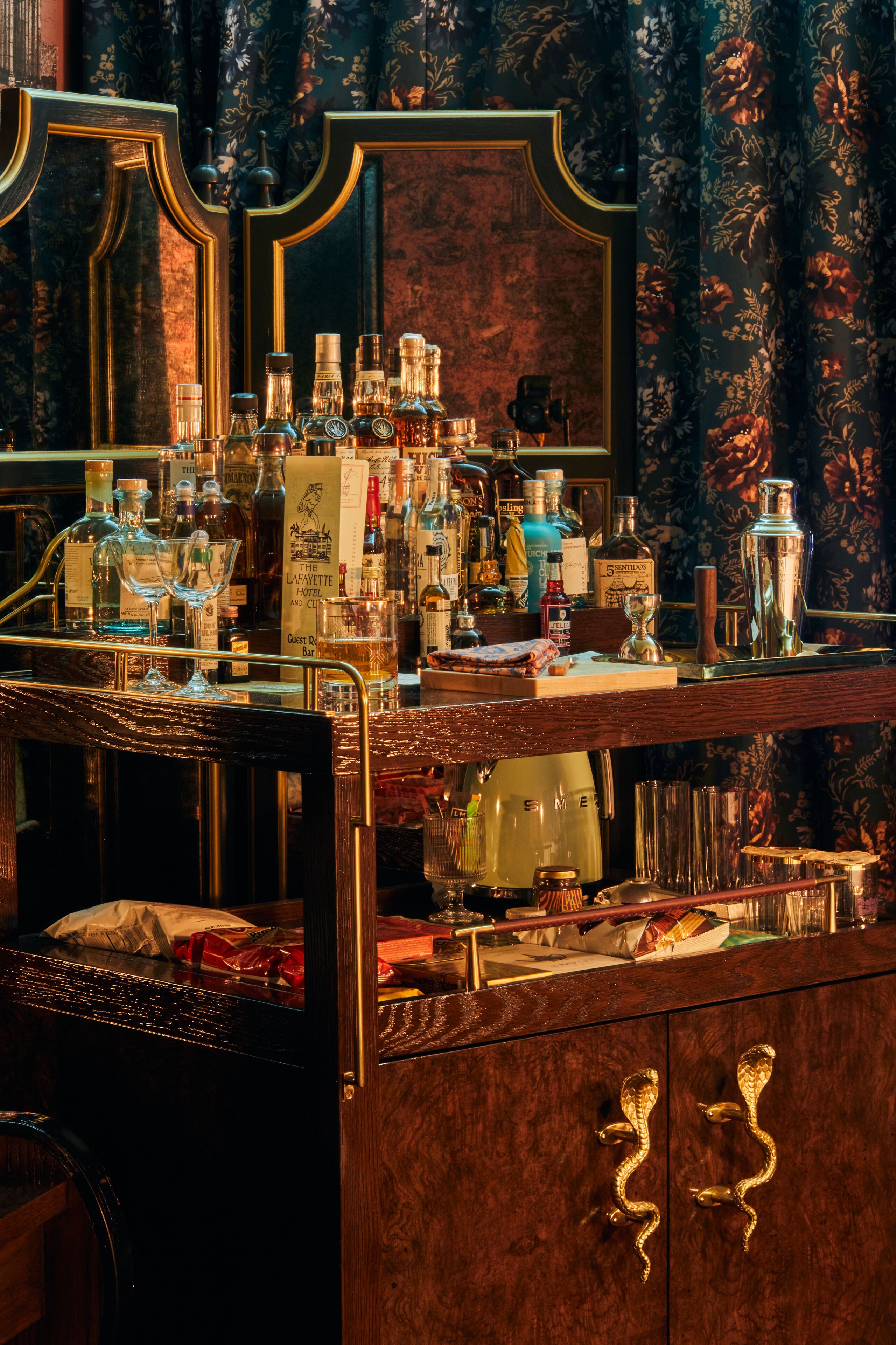 A bar area with a variety of bottles and glasses, a mirror, and a wooden cabinet with drawers.