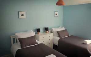 Une chambre double avec deux lits, une table de chevet avec des lampes et des tableaux encadrés au mur.