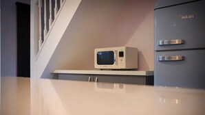 Una cucina con un forno a microonde su un piano di lavoro bianco, un frigorifero grigio con il marchio 'Swan' e una scala con balaustre bianche.