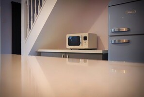 Una cocina con un microondas sobre una encimera blanca, un refrigerador gris con la marca 'Swan' y una escalera de balaustres blancos.