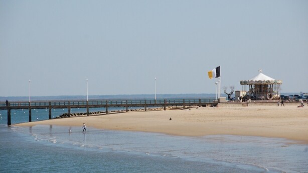 Een strand met een houten steiger, een kiosk en een vlag.