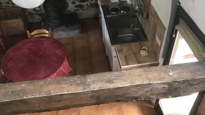 A rustic kitchen with a stone wall, a wooden chair, a red table, and a view of the outside through a window. - Bellchassagne: house  - 2 rooms - 2/3 persons (Bellechassagne)