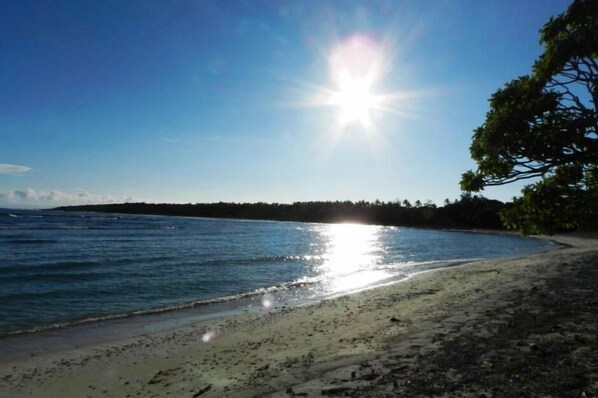 Ein Strand mit blauem Himmel und Sonnenlicht, das sich im Wasser spiegelt.