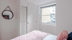 Un dormitorio con cama, ventana, armario y espejo.