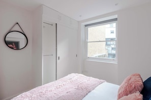 A bedroom with a bed, a window, a wardrobe, and a mirror.
