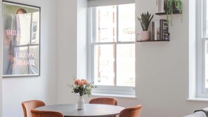 Un comedor con una mesa redonda, cuatro sillas, un jarrón con flores y un sofá con cojines.