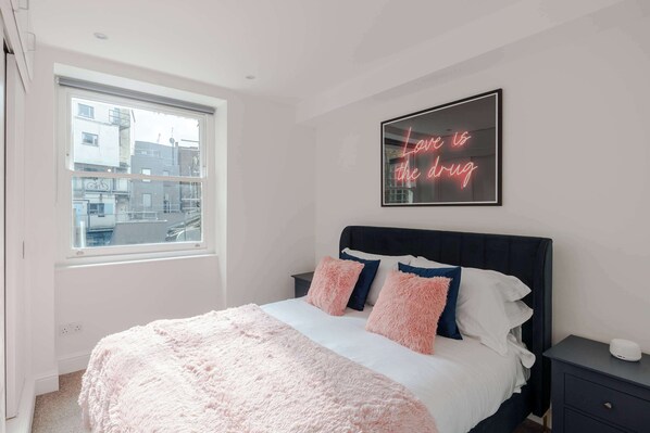 A bedroom with a bed, a window, a neon sign, and a nightstand.