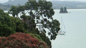 Un paisaje costero con un velero en aguas tranquilas, rodeado de abundante vegetación y montañas lejanas.