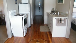 Una cocina compacta con electrodomésticos blancos, piso de madera y una pequeña isla con hervidor.