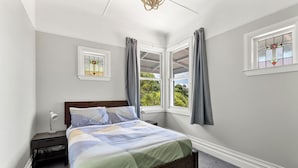 Un dormitorio con cama, mesita de noche, ventana con cortinas y vista a zonas verdes.