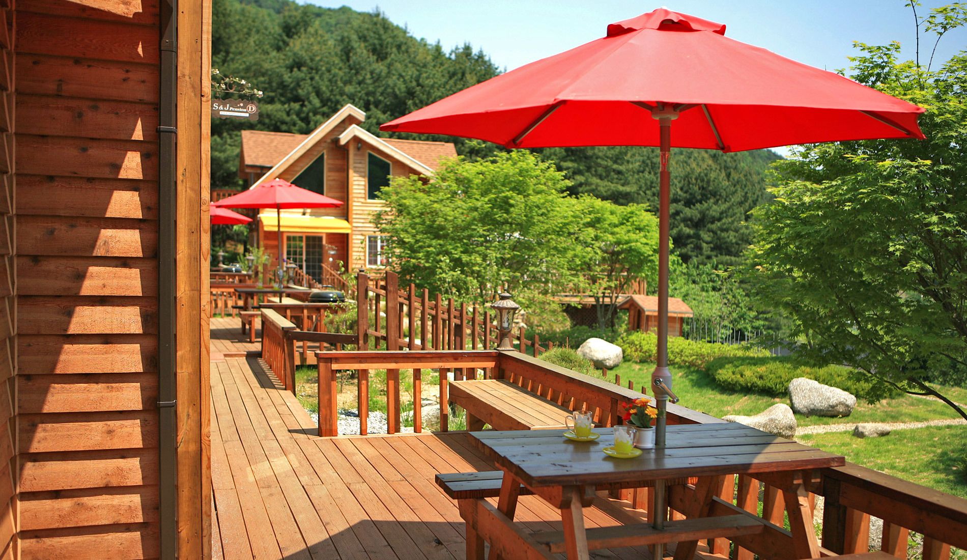 A wooden deck with outdoor seating and red umbrellas.