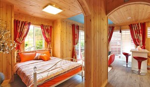 A wooden cabin with a bed, red curtains, and a small bar area with red chairs. - S & J Pension (Gapyeong)