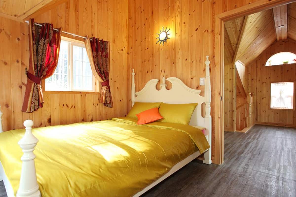 Una habitación de madera con una cama, cortinas y una ventana.