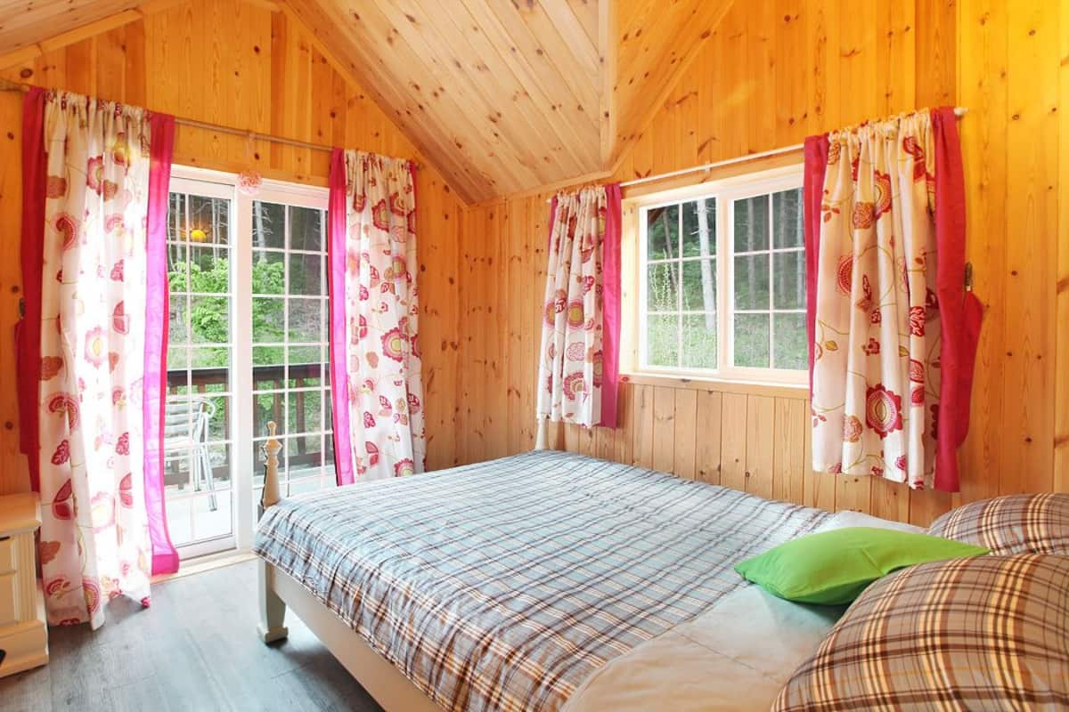 Un dormitorio de cabaña de madera con cama, mesita de noche y cortinas.