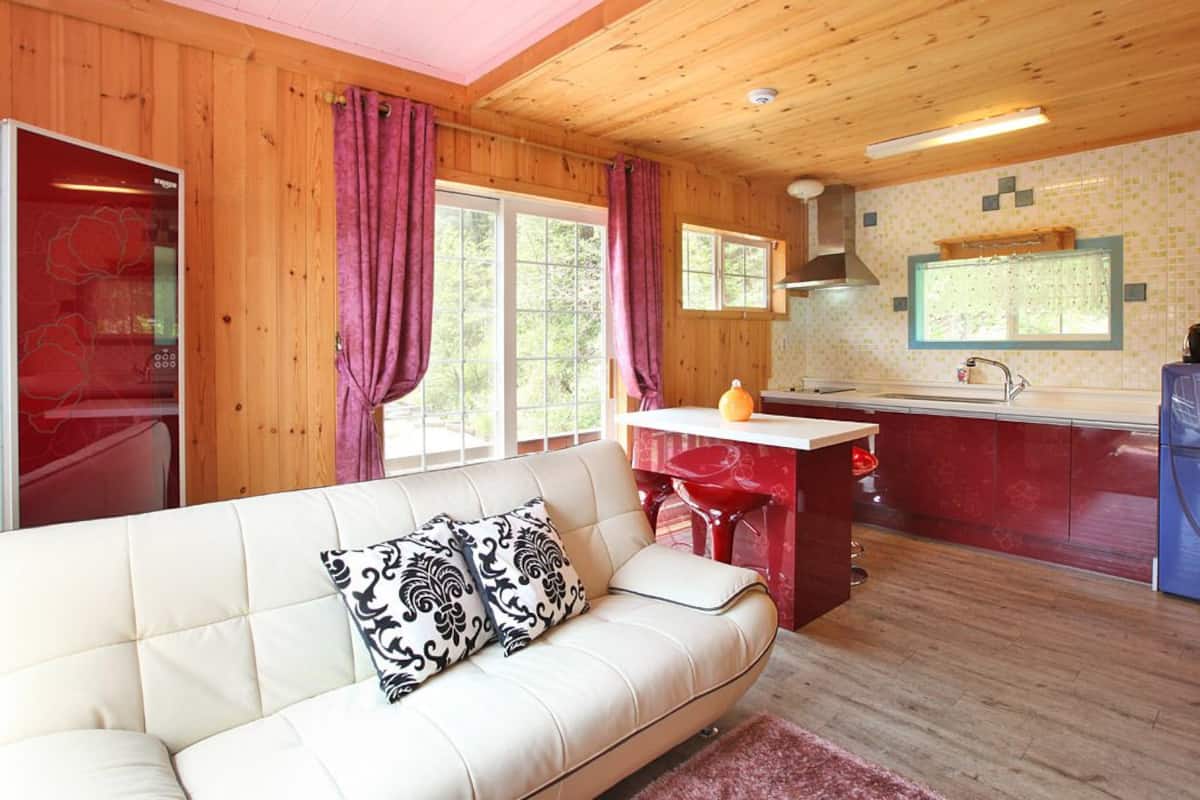 Interior acogedor de una cabaña, con una sala de estar que tiene un sofá blanco y una cocina roja con un fregadero y un refrigerador.