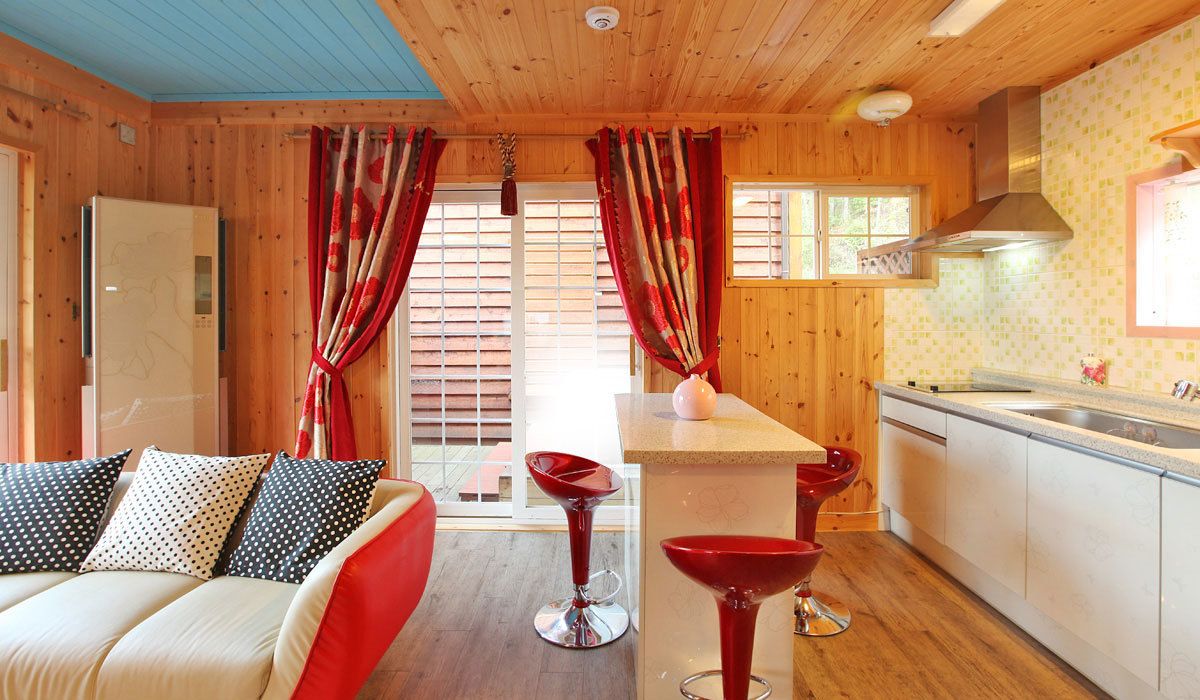 Ein gemütliches Blockhaus mit Holzvertäfelungen, einer Küchenzeile und einer Sitzecke mit einer Couch und zwei roten Barhocker.