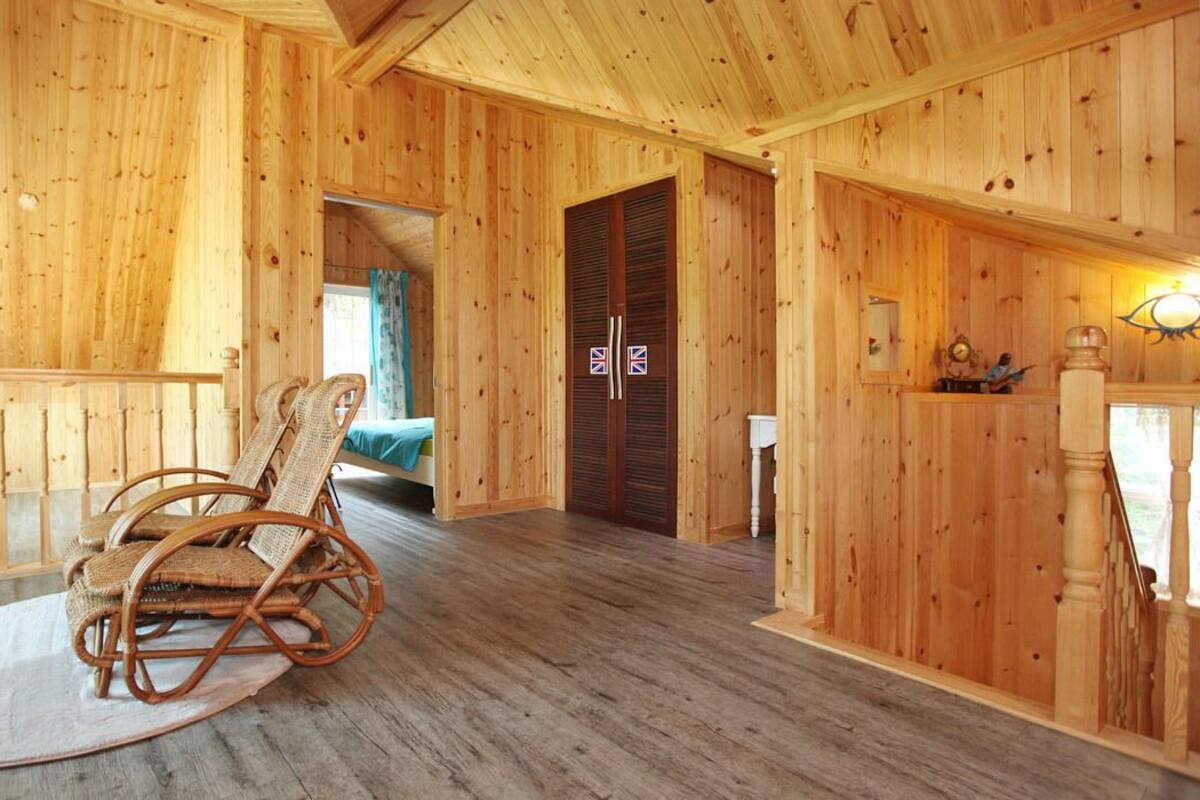 Interior de una cabaña de madera con una mecedora, una cama y una escalera.