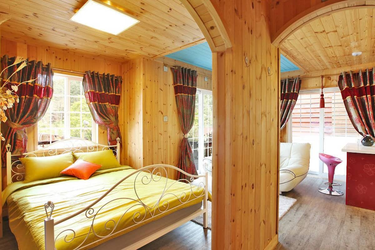 Interior de una cabaña de madera con una cama, una silla y una mesita.