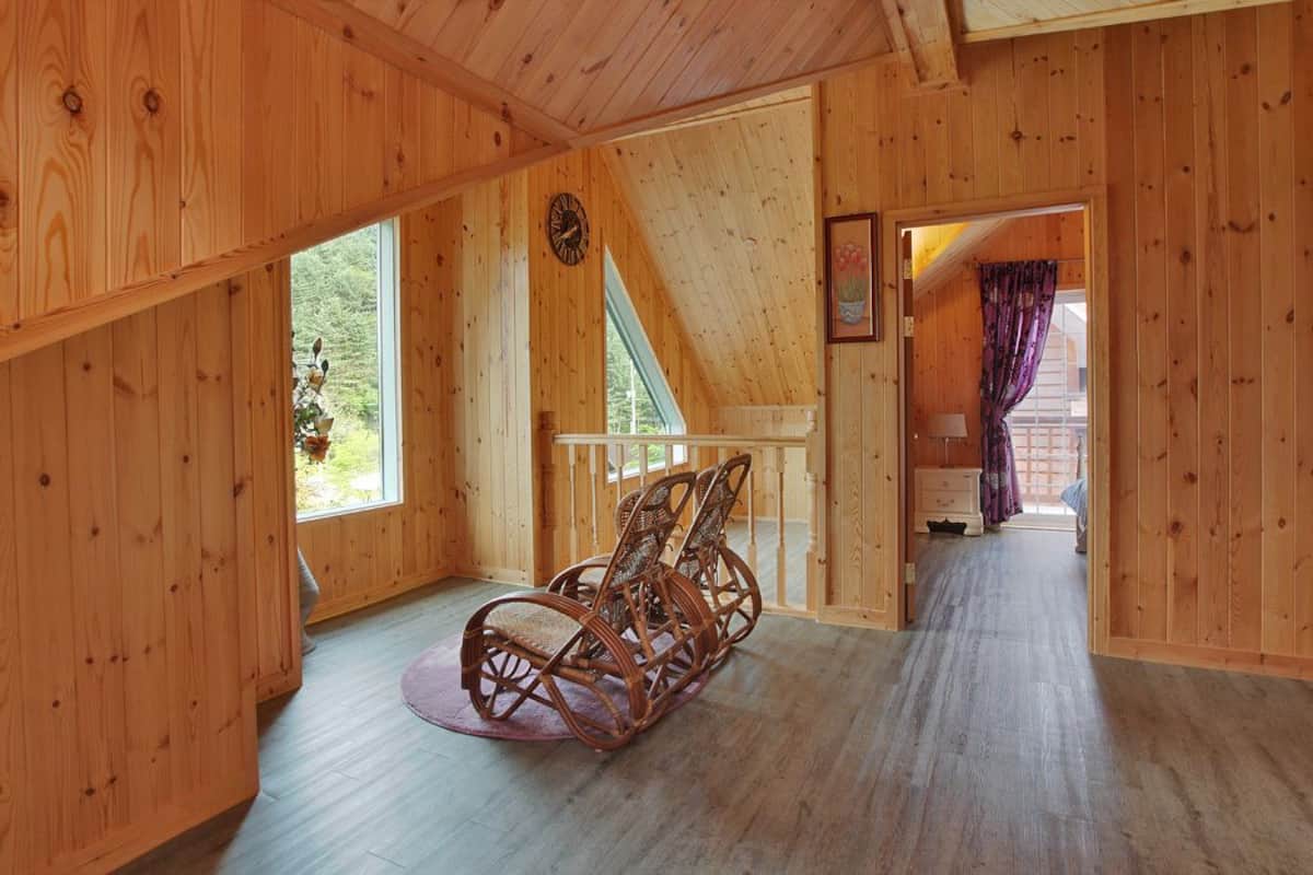 Un interior de madera con una mecedora, una escalera y vistas al verde exterior.