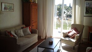 A living room with a sofa, armchair, and a coffee table. There is a wooden cabinet and a window with curtains. - House with large terrace and fenced garden (Saint-Philibert)
