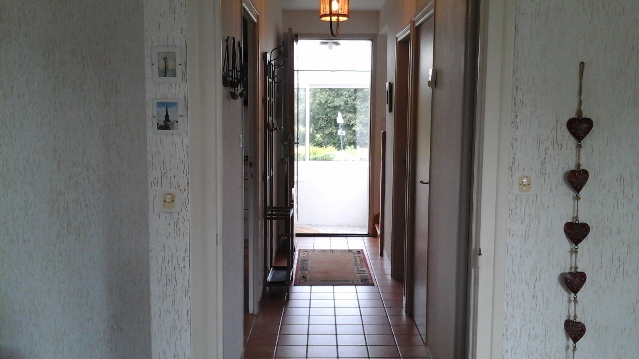 A hallway with a tiled floor, a door at the end, and a wall-mounted light fixture.