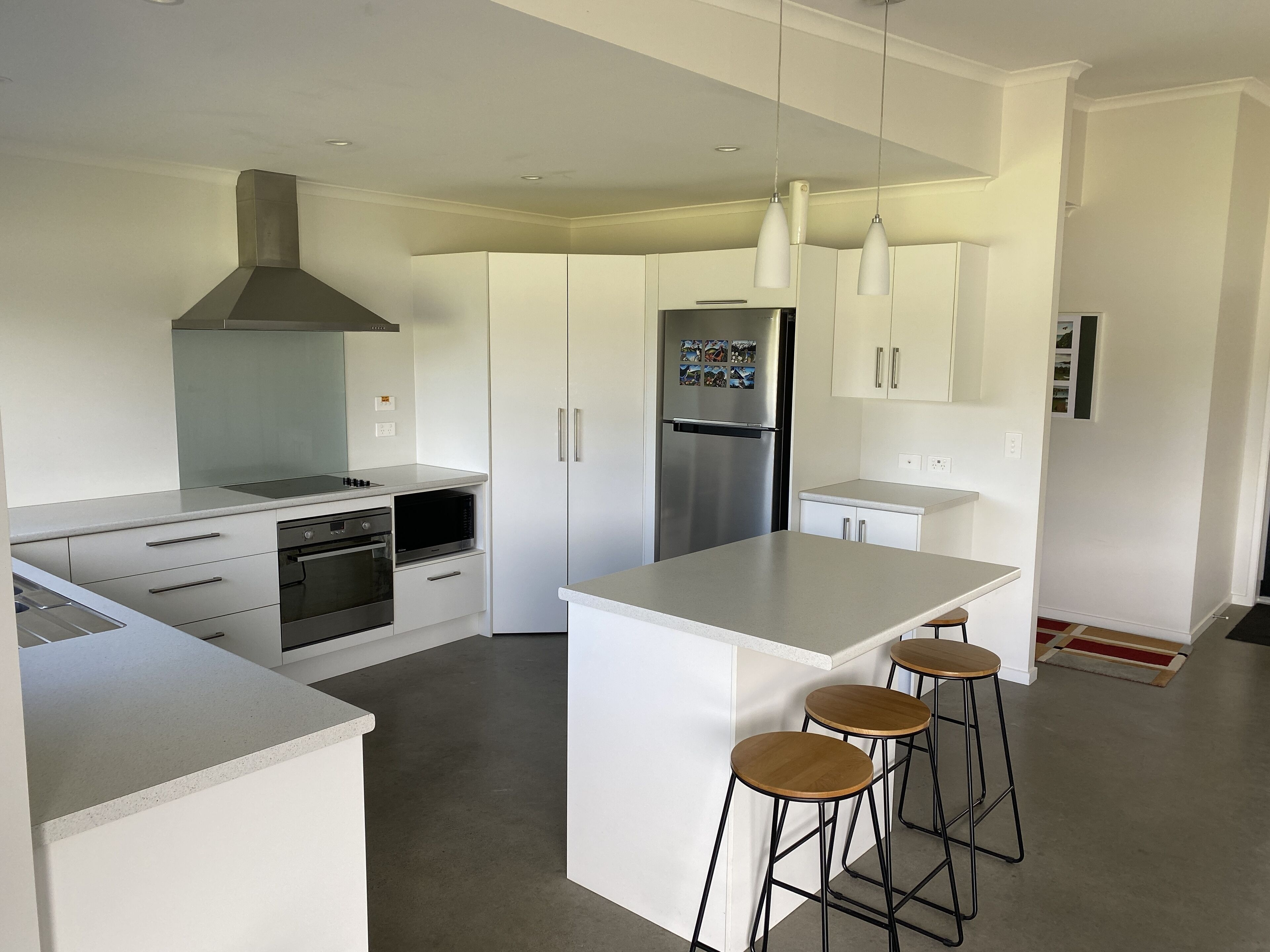 Una cocina moderna con armarios blancos, electrodomésticos de acero inoxidable, una isla central con taburetes y luces colgantes.